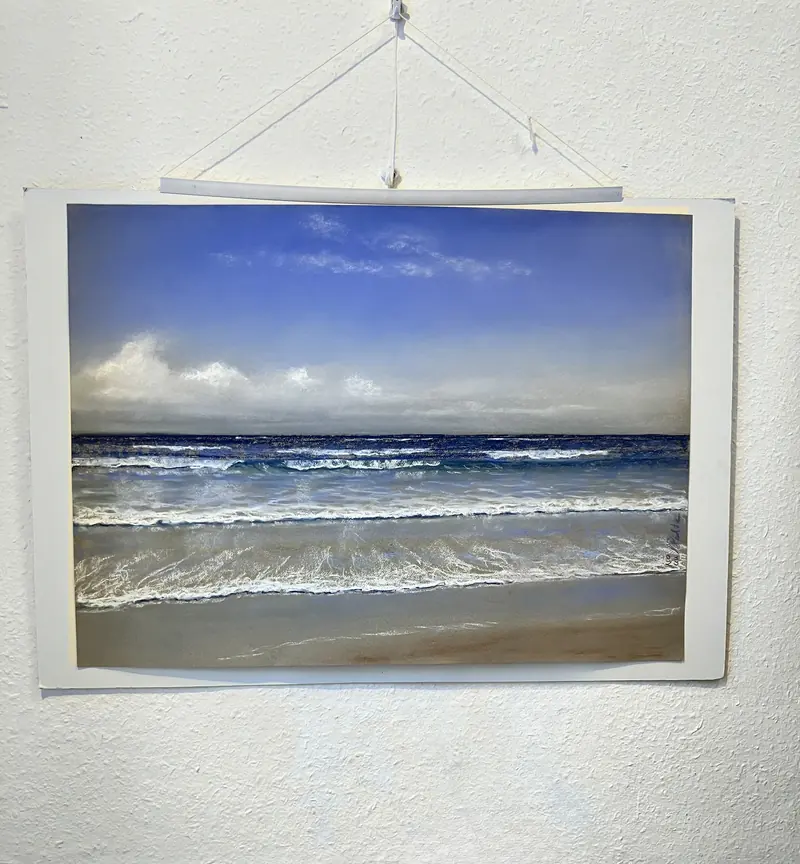 Ein Meeresbild in Pastell hängt an einer weißen Wand
